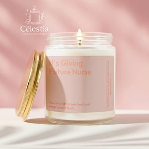 May include: A lit, hand-poured candle in a glass jar with a gold lid. The label reads "It's Giving Future Nurse" with the text "You carry light in your heart and magic in your touch." The candle is on a pink background.