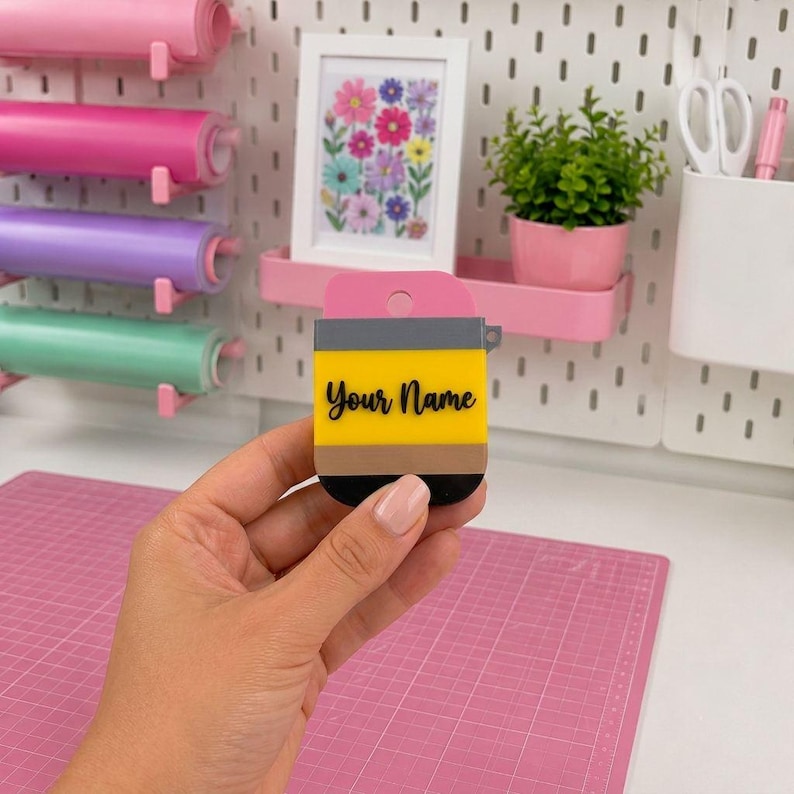 May include: A pencil-shaped silicone case for wireless earbuds featuring a yellow body, a pink top, and a black tip. The text "Your Name" is printed in black script across the center of the yellow section. The case includes a small circular cutout.