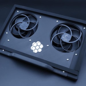 May include: A black rectangular cooling stand featuring two circular fans with black blades and a central silver hexagonal honeycomb logo. The device is constructed with a matte black frame secured by visible silver screws at the corners.