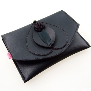 K&ouml;nnte beinhalten: Eine schwarze Lederclutch mit einem dekorativen Blumendesign. Die Blume ist aus schwarzem Stoff und hat eine dunkelgr&uuml;ne Mitte.