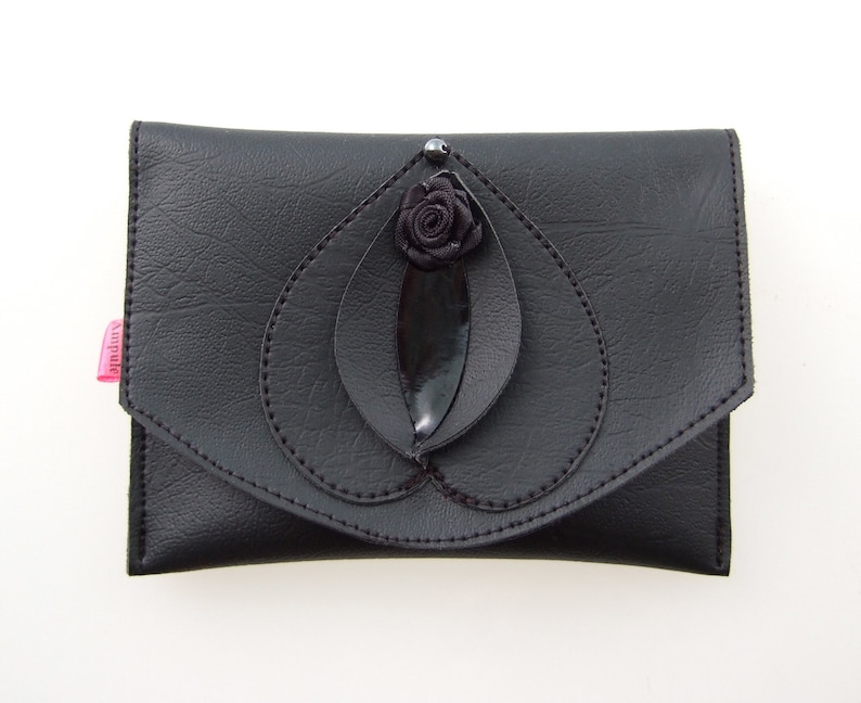 K&ouml;nnte beinhalten: Eine schwarze Leder-Clutch mit einer schwarzen Stoffrose und einer Blattverzierung.