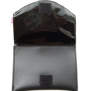 K&ouml;nnte beinhalten: Schwarze Ledertasche mit Klappenverschluss und zwei Klettverschl&uuml;ssen. Die Tasche ist offen und das Innere ist mit schwarzem Stoff ausgekleidet.