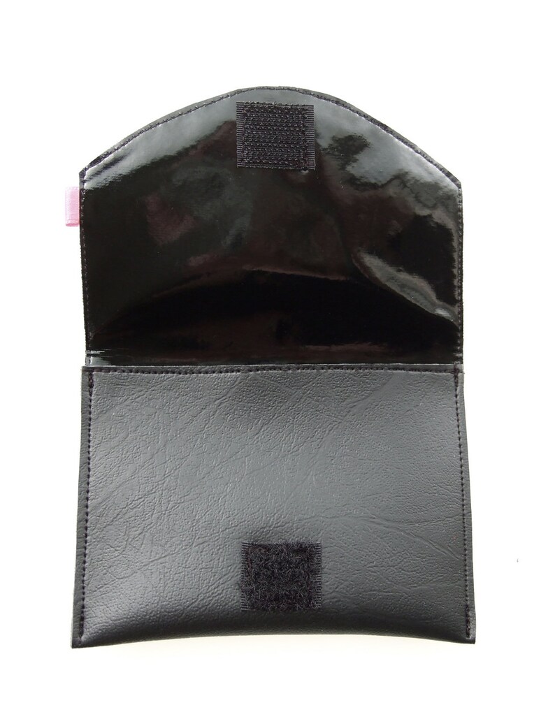 K&ouml;nnte beinhalten: Schwarze Ledertasche mit Klappenverschluss und zwei Klettverschl&uuml;ssen. Die Tasche ist offen und das Innere ist mit schwarzem Stoff ausgekleidet.