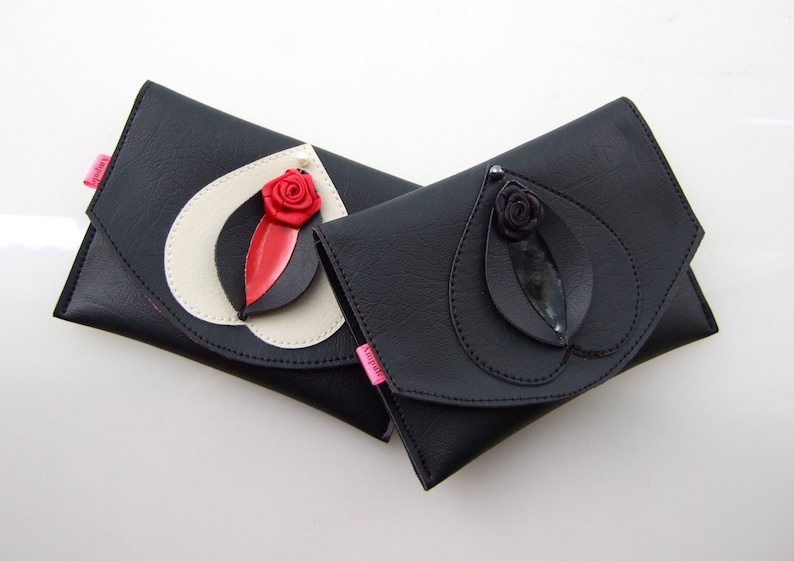 K&ouml;nnte beinhalten: Zwei schwarze Leder-Clutch-Taschen mit einem Blatt- und Blumendesign. Eine Clutch hat eine rote Blume und die andere eine schwarze Blume.