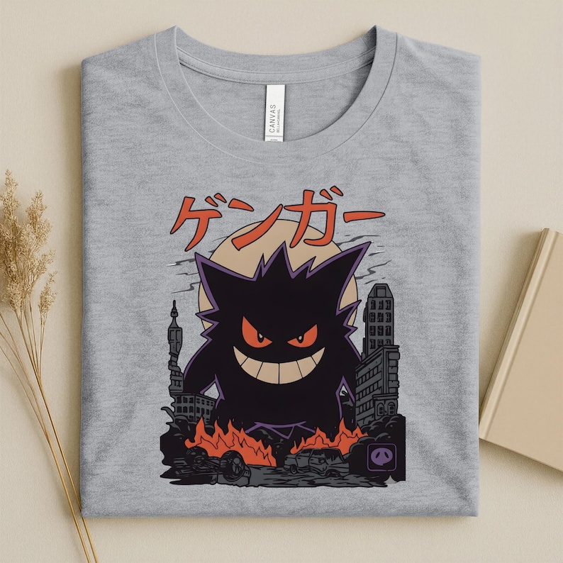 May include: A light gray t-shirt featuring a graphic of a purple monster with red eyes and a wide grin, set against a cityscape with flames. Japanese text is above the monster.
