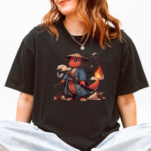 May include: Black t-shirt featuring a cartoon character in a samurai outfit. The character is red with a flame on its tail, wearing a blue robe and a straw hat, holding two swords. The design includes butterflies and clouds.