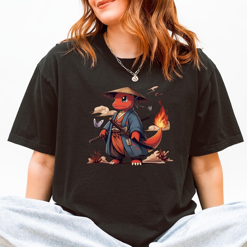 May include: Black t-shirt featuring a cartoon character in a samurai outfit. The character is red with a flame on its tail, wearing a blue robe and a straw hat, holding two swords. The design includes butterflies and clouds.