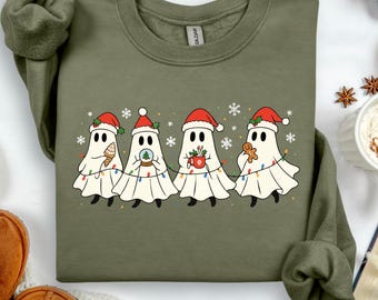 May include: Olive green sweatshirt featuring a festive design of four cartoon ghosts wearing Santa hats and holding holiday items. Each ghost is adorned with string lights and snowflakes, creating a cheerful Christmas theme.