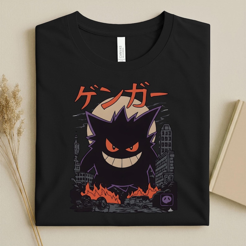 May include: Black t-shirt featuring a purple Gengar graphic with orange eyes and a wide grin, set against a cityscape with flames and the Japanese text "ゲンガー". The design includes a full moon and buildings.