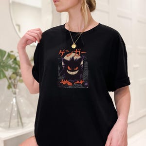 May include: Black t-shirt featuring a Gengar graphic. The design includes the Japanese characters "ゲンガー" above a silhouette of Gengar with a city backdrop and flames. The shirt is a comfortable, casual style.