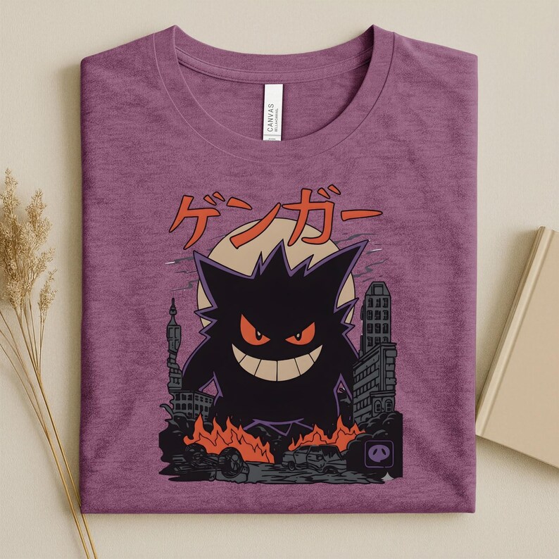 May include: Purple t-shirt featuring a black Gengar graphic with red eyes and a wide grin, destroying a city. Japanese text "ゲンガー" is above the character. The design includes a full moon and burning cars.