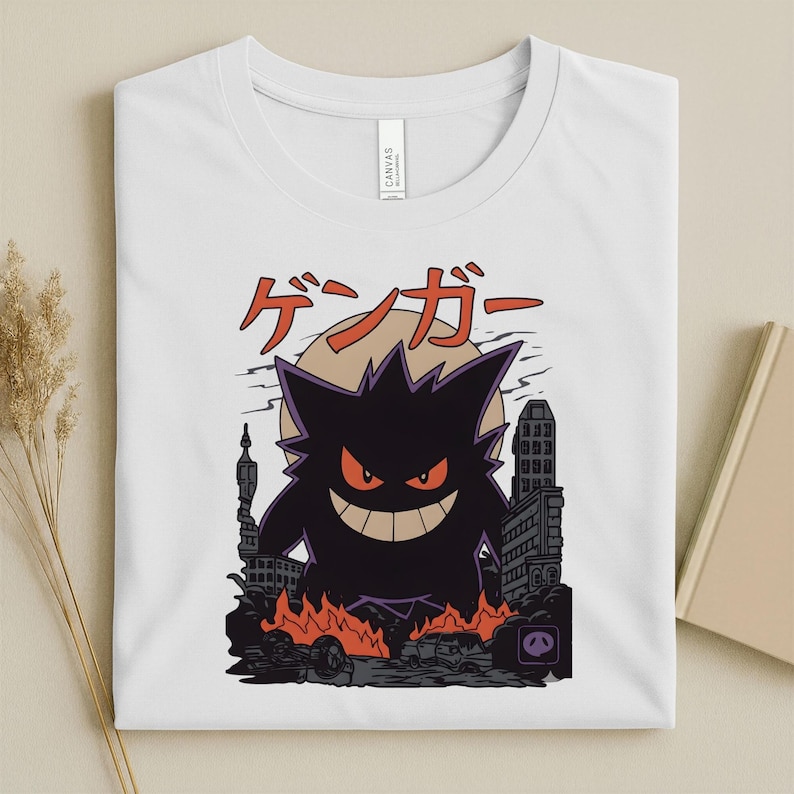 May include: White t-shirt featuring a black cartoon monster with red eyes and a wide grin, standing in a city with flames and the Japanese text "ゲンガー" above. The design is a graphic illustration.