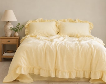 May include: A light yellow bedding set featuring a duvet cover and two matching pillowcases, all adorned with ruffled edges. The fabric has a subtle, textured appearance, and the set is arranged neatly on a bed with a neutral-colored wall behind.