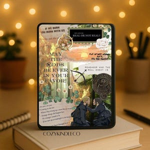 May include: A Kindle case featuring a collage design with text and imagery from a popular book series. The case includes quotes, a bow and arrow, and a sunset scene. The case is resting on a book.