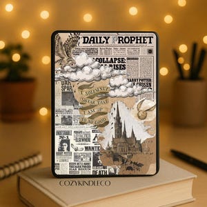 Op de afbeelding: Een zwarte e-reader hoes met een krantenontwerp, met de tekst "DAILY PROPHET" en illustraties van een uil, wolken en een kasteel. De hoes ligt op een stapel boeken, met pennen en een bril in de buurt.