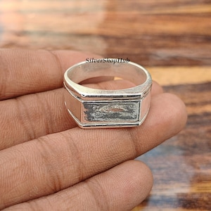 Peut inclure: Une bague en argent dotée d'une surface supérieure plate et rectangulaire avec une finition polie. L'anneau présente un design large et lisse. Le texte SilverShopHub est visible au-dessus de la bague, présentée de manière claire.