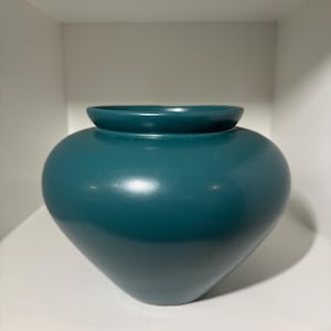 May include: Teal-colored ceramic vase with a rounded body and a small, circular opening. The vase has a smooth, glossy finish and a simple, elegant design. The vase is a decorative item.