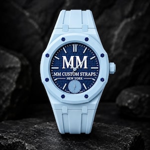 Könnte beinhalten: Eine hellblaue Armbanduhr mit einem dunkelblauen, texturierten Zifferblatt, das den weißen Schriftzug MM, MM CUSTOM STRAPS und NEW YORK zeigt. Die Uhr hat eine hellblaue Lünette mit dunkelblauen Schrauben, ein passendes Armband und ein kleines Hilfszifferblatt.