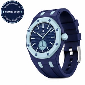 Könnte beinhalten: Eine blaue und hellblaue Armbanduhr mit strukturiertem Zifferblatt und passendem blauen Armband. Das Zifferblatt trägt die Aufschrift "AP x Swatch" und "Royal Pop". Die Uhr hat einen silbernen Verschluss und eine hellblaue Lünette.