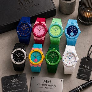 Puede incluir: Ocho relojes de pulsera con correas de silicona en varios colores, incluyendo azul, rosa, verde lima, azul claro, negro, amarillo, verde y blanco. Los relojes cuentan con esferas redondas con el texto MM CUSTOM STRAPS AU y biseles plateados.