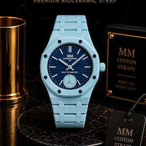 May include: A light blue bioceramic watch with a dark blue textured dial, featuring the text MM CUSTOM STRAPS AU and BUILT TO STAND OUT. The watch has a matching light blue link strap and a small sub-dial labelled Royal Pop at the bottom.