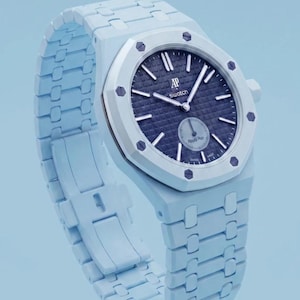 Könnte beinhalten: Eine hellblaue Armbanduhr mit einem dunkelblauen, texturierten Zifferblatt, silbernen Zeigern und Indizes. Das Zifferblatt zeigt den Text AP, Swatch und Royal Poo. Sie hat eine achteckige Lünette mit acht sichtbaren Schrauben und ein passendes Gliederarmband.