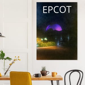Peut inclure: Une impression murale verticale représentant une scène nocturne de la sphère géodésique d'Epcot illuminée par une lumière violette vive. Le mot EPCOT est imprimé en grandes lettres capitales blanches dans le ciel sombre au-dessus de la structure.