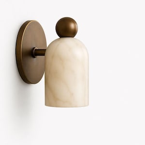 Può includere: Applique da parete con paralume cilindrico in marmo bianco sporco con venature marroni, sormontato da un piccolo accento rotondo color bronzo. Il paralume è collegato a un supporto a parete circolare in bronzo tramite un braccio corto e dritto.