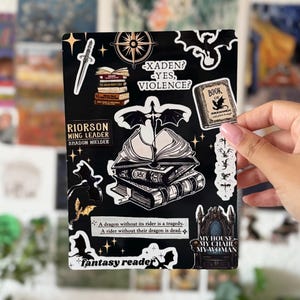 Könnte beinhalten: Ein schwarzer, rechteckiger Aufkleberbogen mit verschiedenen Fantasy-Illustrationen, darunter ein Bücherstapel, ein Schwert, ein Kompass, ein Drache und ein Thron. Der Text umfasst "Xaden? Yes, violence?", "Riorson Wing Leader" und "My house, my chair, my woman."