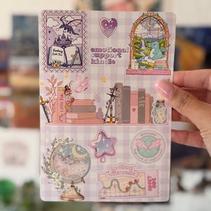 Könnte beinhalten: Ein Stickerbogen mit Fantasy-Illustrationen auf einem hellvioletten Vichy-Karo-Hintergrund. Die Motive umfassen einen Drachen, ein Schloss, Bücher, einen Globus, einen Stern sowie den Text "emotional support kindle" und "Rhysand".