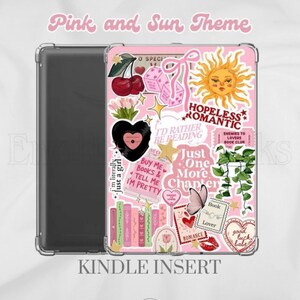 Op de afbeelding: Een doorzichtige Kindle-hoes met een roze inzetstuk versierd met diverse stickers, waaronder een zon, kersen, een zwart hart, boeken, een vlinder en teksten zoals Hopeless Romantic, Just One More Chapter en I'd Rather Be Reading.