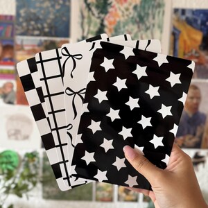 Könnte beinhalten: Ein Set aus vier rechteckigen Karten mit verschiedenen schwarz-weißen Mustern. Die Designs umfassen ein Schachbrettmuster, ein Gittermuster, eine Reihe schwarzer Schleifen auf weißem Grund und einen schwarzen Hintergrund mit weißen Sternen.