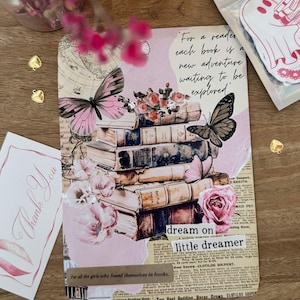 Puede incluir: Una impresión estilo collage con una pila de libros antiguos, rosas rosas y mariposas. El texto "For a reader each book is a new adventure waiting to be explored" es visible. El texto adicional incluye "dream on little dreamer".