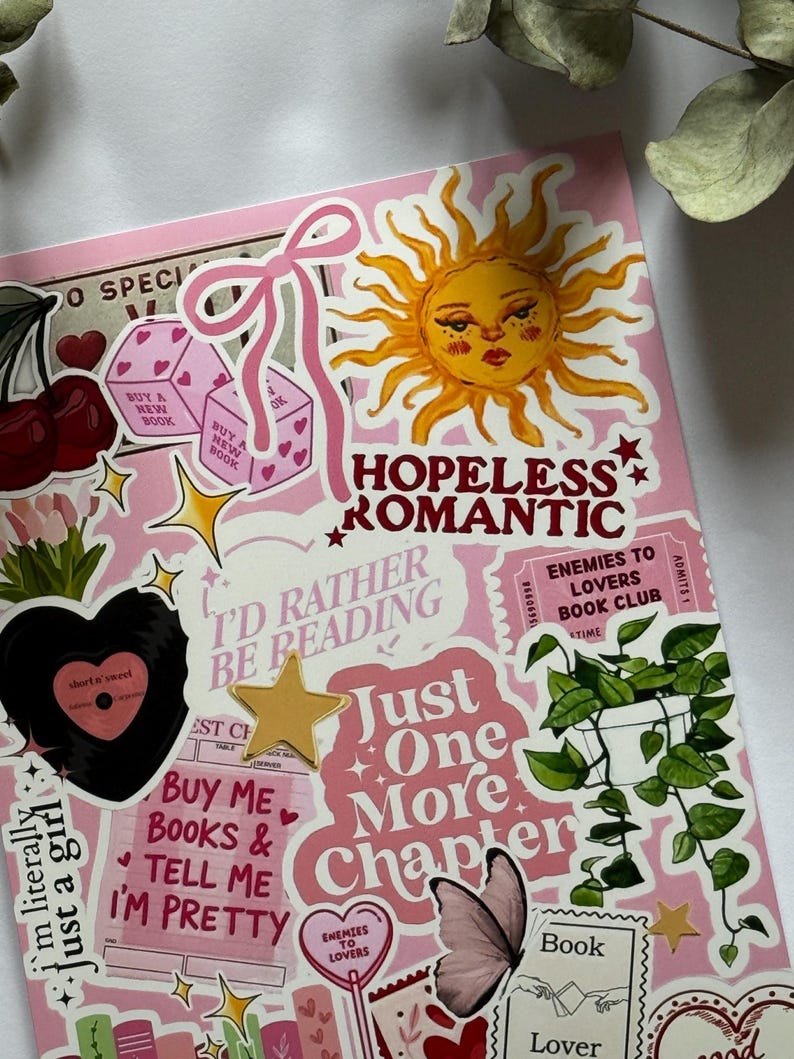 Op de afbeelding: Een roze oppervlak bedekt met diverse stickers, waaronder een gele zon, een roze strik, kersen, dobbelstenen, een zwarte vinylplaat, een kamerplant, een vlinder en tekst met "HOPELESS ROMANTIC", "I'D RATHER BE READING" en "Just One More Chapter".