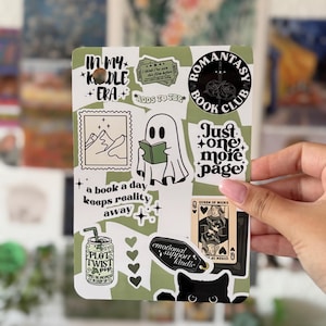 Può includere: Un foglio di adesivi rettangolare con vari disegni a tema libro in tonalità verde salvia, nero e bianco. Le illustrazioni includono un fantasma che legge, una carta da gioco, un gatto e testi come In my Kindle Era e Romantasy Book Club.