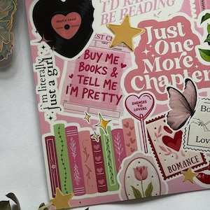 Op de afbeelding: Een verzameling stickers in roze en rode tinten met illustraties van boeken, een vinylplaat, vlinders, tulpen en sterren. De tekst bevat "I'd rather be reading", "Just one more chapter", "Buy me books & tell me I'm pretty" en "Enemies to lovers".