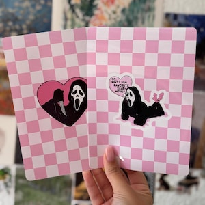 Könnte beinhalten: Zwei rechteckige Karten mit einem hellrosa-weißen Karomuster. Die linke Karte zeigt eine schwarze Ghostface-Figur in einem rosa Herz. Die rechte Karte zeigt eine Ghostface-Figur mit einer Sprechblase mit dem Text SO... WHAT'S YOUR FAVORITE SCARY MOVIE?