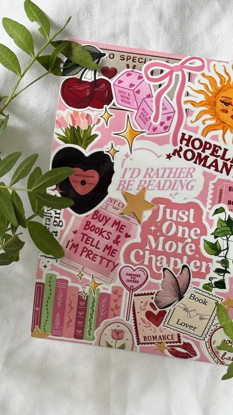 Op de afbeelding: Een roze collage met diverse stickers waaronder kersen, dobbelstenen, een zon, een zwart hart en boeken. De tekst bevat "I'd Rather Be Reading", "Just One More Chapter", "Buy Me Books & Tell Me I'm Pretty", "Enemies to Lovers" en "Book Lover".