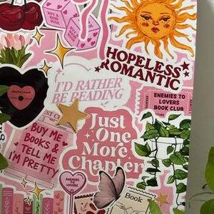 Op de afbeelding: Een rechthoekig roze oppervlak bedekt met diverse stickers met illustraties van een zon, kersen, dobbelstenen, een vlinder, een kamerplant en boeken. De tekst bevat "HOPELESS ROMANTIC", "I'D RATHER BE READING", "Just One More Chapter" en "Book Lover".