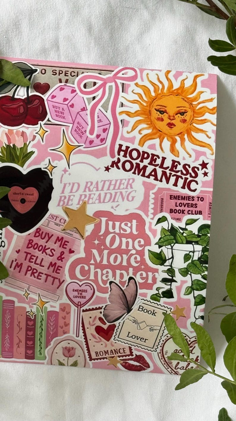 Op de afbeelding: Een rechthoekig roze oppervlak bedekt met diverse stickers met illustraties van een zon, kersen, dobbelstenen, een vlinder, een kamerplant en boeken. De tekst bevat "HOPELESS ROMANTIC", "I'D RATHER BE READING", "Just One More Chapter" en "Book Lover".