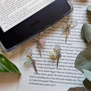 Op de afbeelding: Drie bladwijzers voor een Kindle e-reader, elk voorzien van een kleine zilverkleurige zwaardbedel gecombineerd met een doorschijnende bloemvormige kraal in lichtgroen, zachtroze of lichtgeel, bevestigd aan een doorzichtige plastic clip.