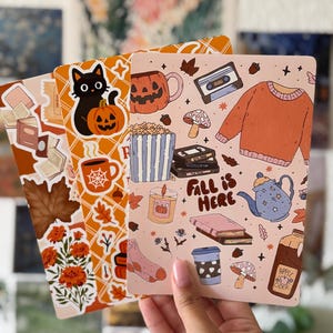 Peut inclure: Trois feuilles d'autocollants rectangulaires avec des illustrations sur le thème de l'automne. Les motifs incluent un chat noir avec une citrouille, des pulls orange, un mug citrouille, des livres, des feuilles, du pop-corn et le texte Fall is Here.