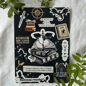 Puede incluir: Hoja de pegatinas negra con ilustraciones de fantasía. Incluye una brújula, una daga, pilas de libros, un dragón y texto que dice "Xaden? Yes, Violence?" y "Fantasy Reader."
