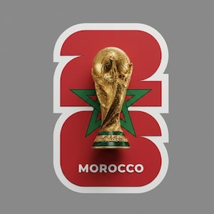 May include: A gold FIFA World Cup trophy sits atop a red and white graphic with the word "MOROCCO" in white. The graphic features the number "23" and a green star, set against a gray background. The trophy is detailed with a globe design.