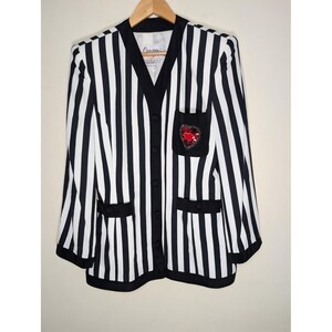 May include: A black and white striped blazer with a black collar, buttons, and pocket details. The blazer features a small pocket with a red heart design. The blazer is hanging on a wooden hanger.