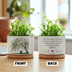 May include: White ceramic planter with a weeping willow tree illustration and a wooden base. The back of the planter has the text "Like the willow, we have learned to bend with the winds of life, always standing strong together."