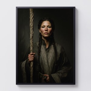 May include: A framed portrait of a woman with dark hair in braids, holding a carved wooden staff. She wears a dark gray robe with ornate detailing. The background is a dark, neutral tone, enhancing the focus on the subject.
