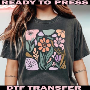 May include: Dark gray t-shirt featuring a floral design with pink, orange, green, and purple flowers and leaves. The words "READY TO PRESS" and "DTF TRANSFER" are printed in pink and black.