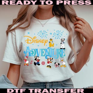 K&ouml;nnte beinhalten: Wei&szlig;es T-Shirt mit dem Schriftzug "Disney Adventure" in Blau und Gelb, mit Zeichentrickfiguren wie Mickey Mouse, Minnie Mouse, Donald Duck und Pluto. Das Design beinhaltet Feuerwerk und Sterne.