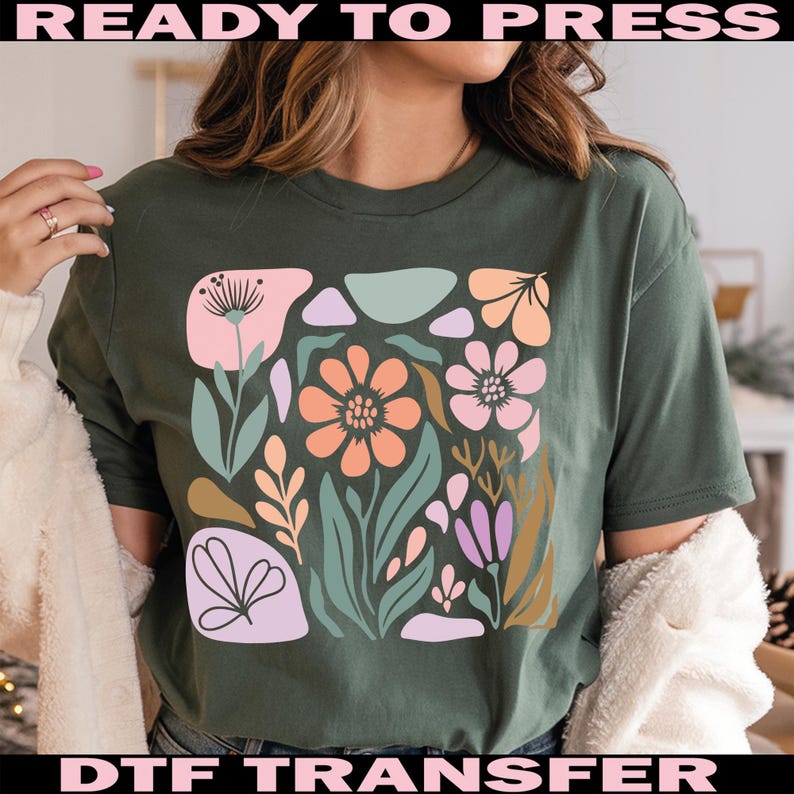 May include: Dark green t-shirt featuring a floral design in a square. The design includes flowers in shades of pink, orange, and purple, with green leaves and stems. The words "READY TO PRESS" and "DTF TRANSFER" are printed on the top and bottom.